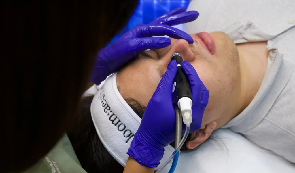 Practitioner in gloves performing a facial skin treatment on a client at loom:aesthetics