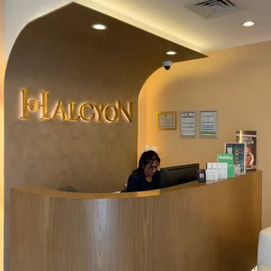 Reception desk at Halcyon Aesthetics Clinic with the Halcyon logo on the wall and a receptionist